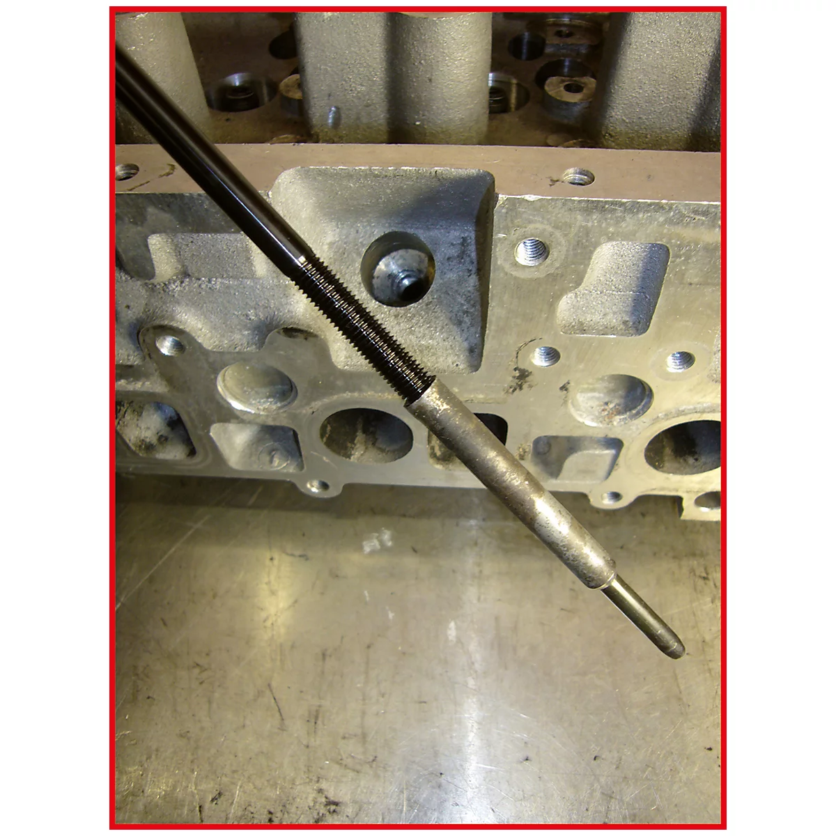 Nahaufnahme einer Zündkerze, die in den Zylinderkopf eingesetzt wird. Der Kopf und die Werkzeuge bestehen aus Metall.